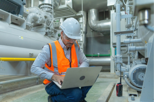 worker in safety gear on a computer in industrial space